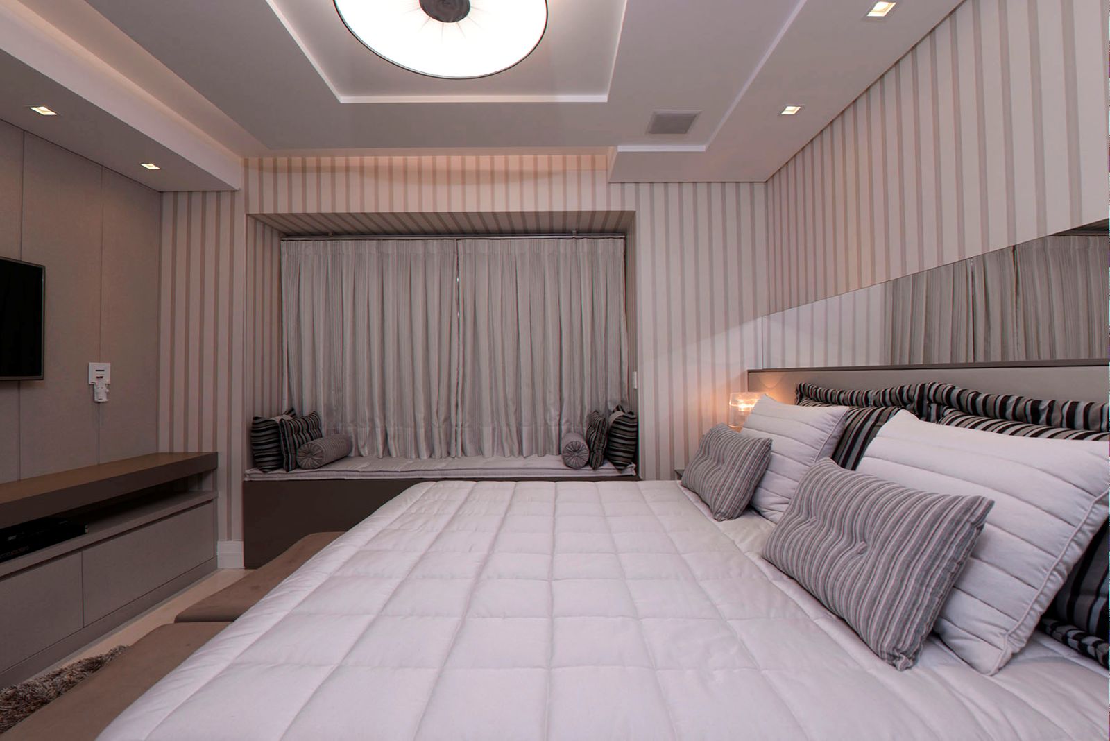 Quarto com cortina de voil no recanto da janela, papel de parede listrado e almofadas